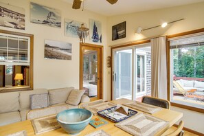 A cozy living room with a sofa, a dining table with placemats, a large bowl, and artwork on the walls. - 4,200 Sq Ft Mid-cape Cottage w/ Furnished Deck! (Brewster)