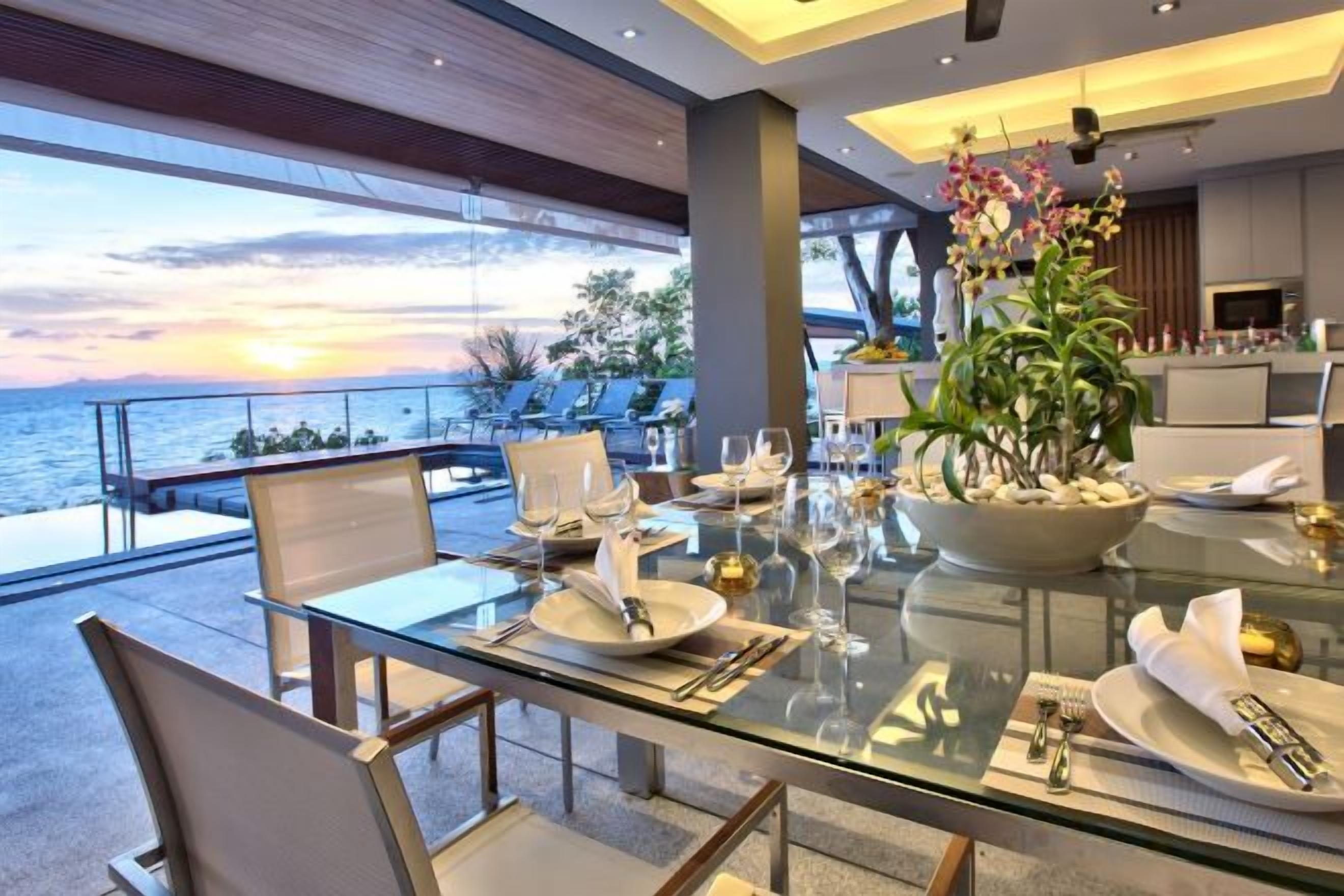 A dining area with a glass table, chairs, and a view of the sea.