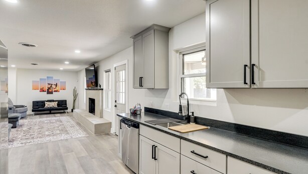 A modern kitchen with grey cabinets, a black countertop, and a dishwasher. - Backyard & Game Room! Home in Heart of Midland (Midland)