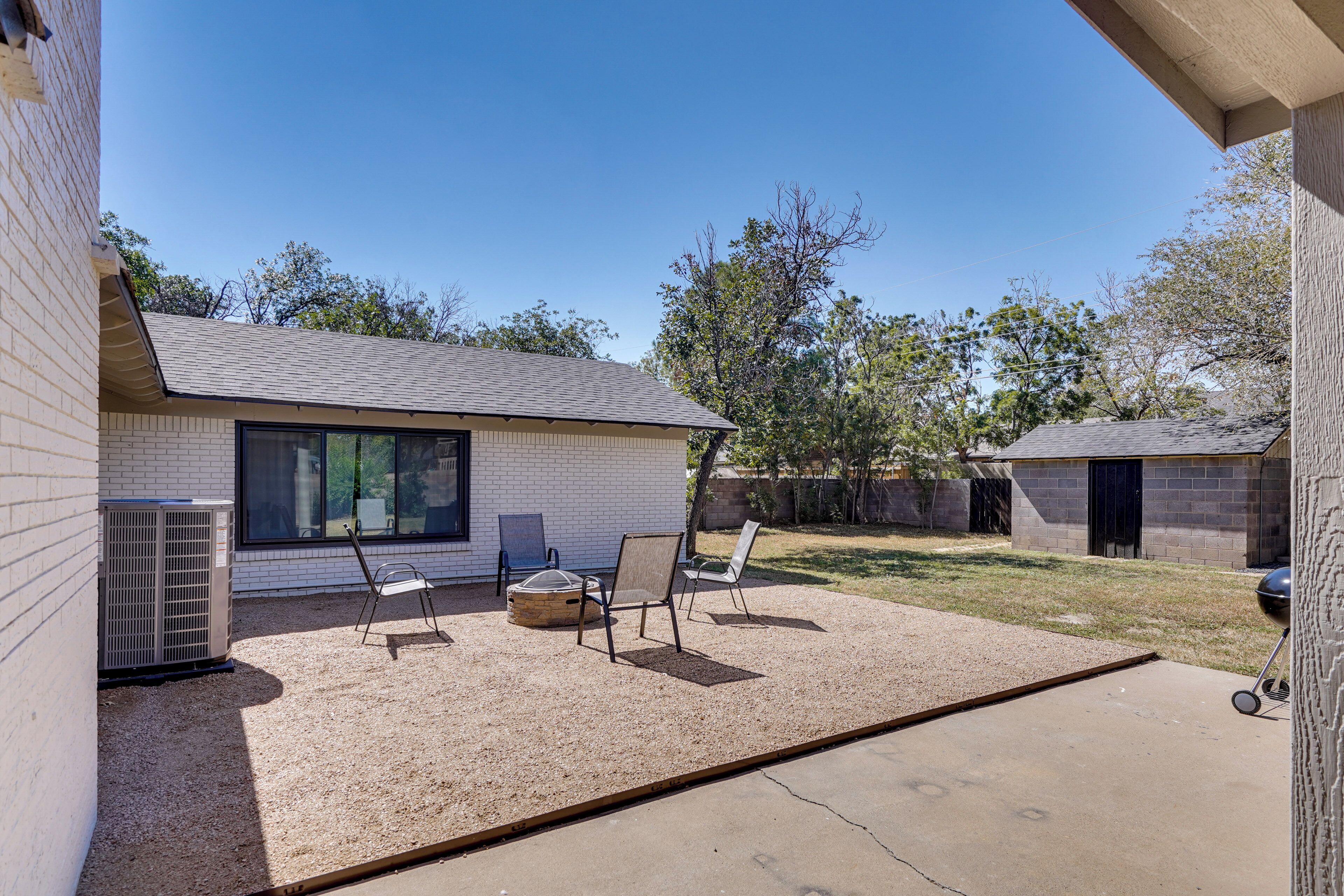 A residential backyard with a patio, two chairs, a grill, and a brick house.