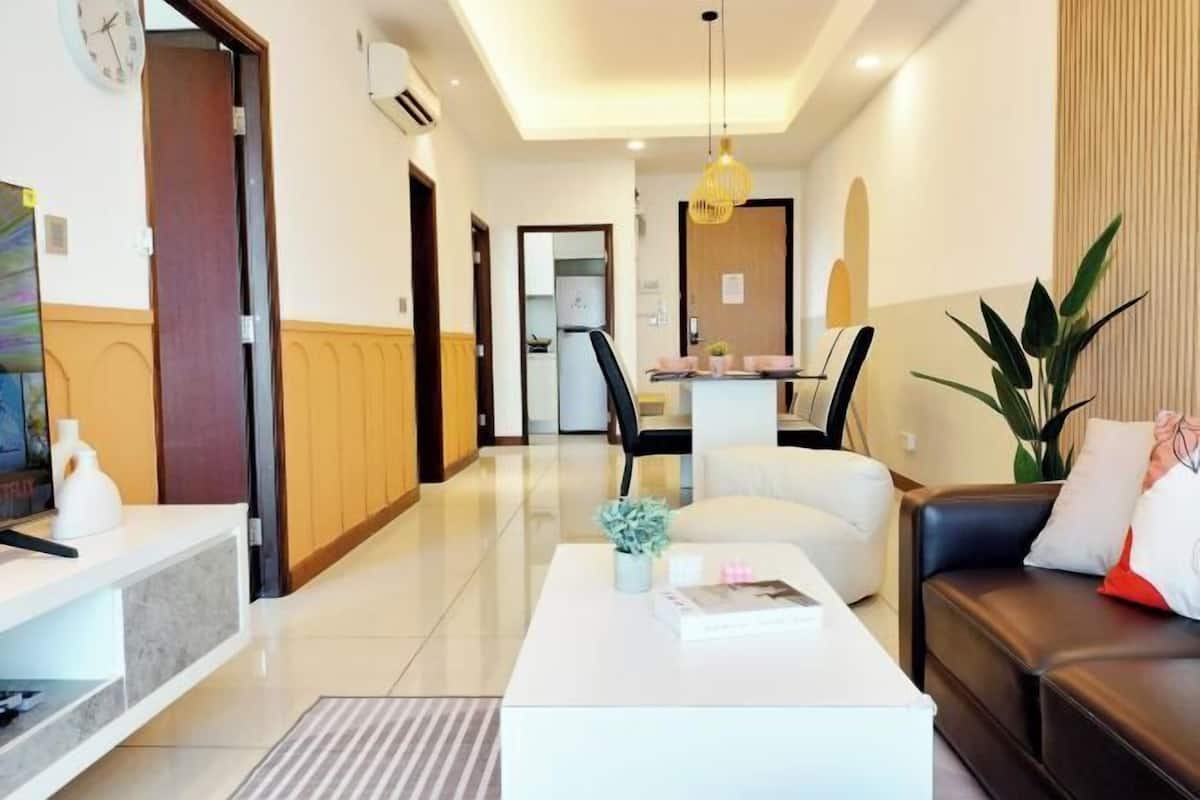 A modern living room with a white coffee table, a black leather sofa, and a dining area in the background.