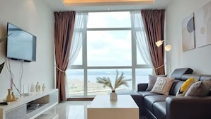 A modern living room with a large window, a flat-screen TV, a sofa, and a coffee table. - Delight Homestay Paragon Residences (Johor Bahru)