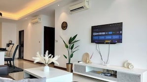 A modern living room with a flat-screen TV, a white entertainment unit, a potted plant, and a minimalist design. - Delight Homestay Paragon Residences (Johor Bahru)