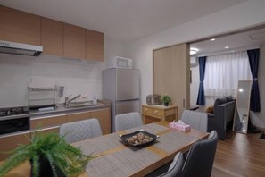 A compact kitchen with modern appliances, a dining area with a table and chairs, and a living area with a sofa and a mirror.