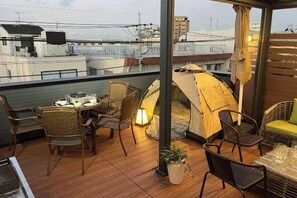 Una terraza en la azotea con una mesa redonda, sillas, una tienda de campaña y vistas de la ciudad.