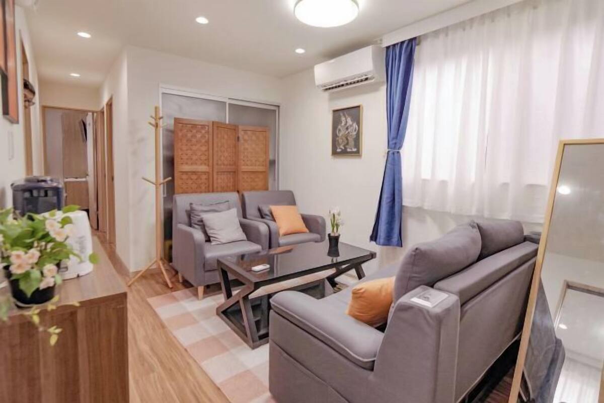 Una sala de estar moderna con un sofá, una mesa de centro y un televisor. Se aprecia un armario, una planta y una ventana con cortinas.
