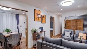 A modern living room with a sofa, a dining area with a table and chairs, and a kitchen area with a coffee machine.