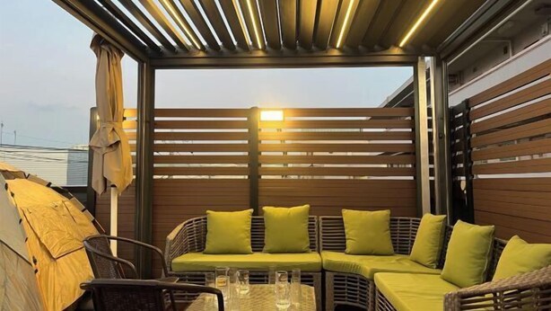 A covered outdoor seating area with a sofa and chairs, a table with glasses, and a tent.