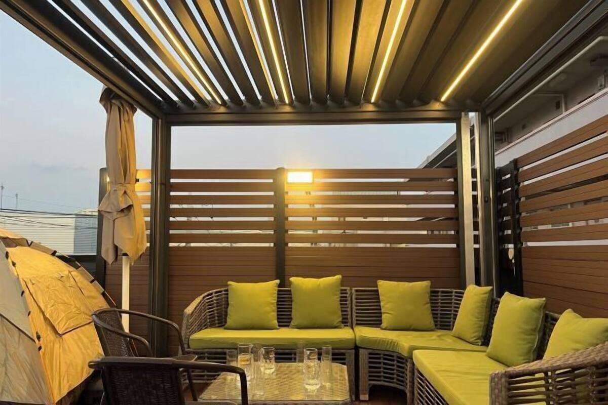Un espacio de estar techado al aire libre con un sofá, sillas, una mesa con vasos y una carpa.