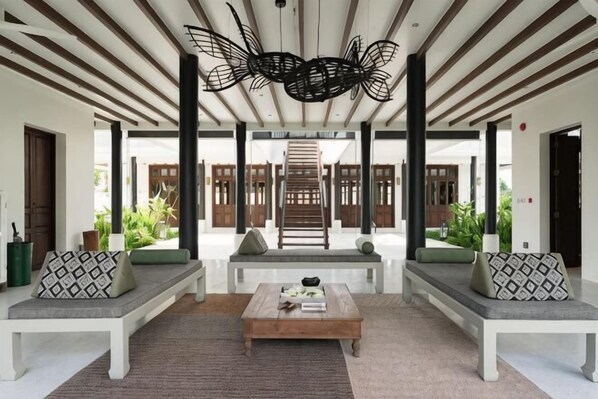 A covered outdoor seating area with benches and a coffee table, surrounded by wooden pillars and a decorative ceiling light.