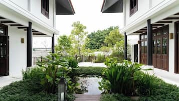 A white building with a covered walkway, surrounded by lush greenery and a small water feature.