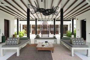 Un espace intérieur spacieux avec un escalier central, deux coins salon dotés de coussins à motifs et une table basse.