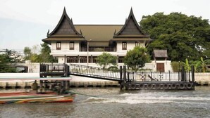Un bâtiment traditionnel avec un pont enjambant une étendue d’eau, un bateau et une petite construction sur le pont.