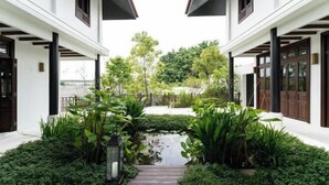 Un bâtiment blanc doté d’une allée couverte, d’une végétation luxuriante et d’un petit élément décoratif aquatique.