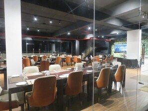 Un salón de conferencias con varias mesas y sillas, paredes de vidrio y un moderno diseño de techo.
