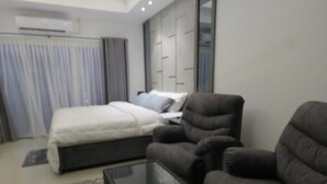A modern hotel room with a bed, a dark armchair, a glass coffee table, and a wardrobe with a mirror. - COASTAL COCOON STUDIO NEGOMBO (Negambo)