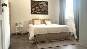 Ein Schlafzimmer mit einem Bett, einem Nachttisch, einem Wandbild, einer Heizung und einem Fenster mit Vorhängen.