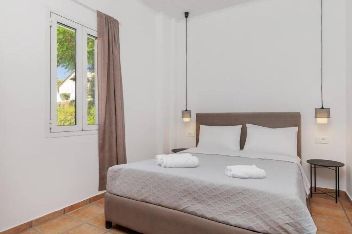 A bedroom with a bed, two bedside lamps, a window with curtains, and a small table.
