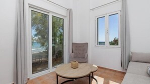 A room with a large sliding glass door, a round table with a woven basket, a grey armchair, and a sofa. - Aliki's Summerhouse 2 (Argassi)