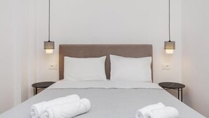 A neatly made bed with white linens and two rolled towels, a wooden headboard, and two bedside tables with wall-mounted lamps. - Aliki's Summerhouse 2 (Argassi)