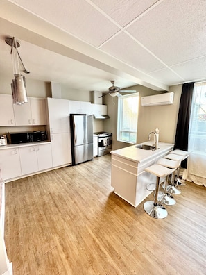 A modern kitchen with white cabinets, stainless steel appliances, a wooden floor, and a window with a view. - Ideal stay, 3 ½-room apartment in the heart of downtown Trois-Rivières (Trois-Rivières)