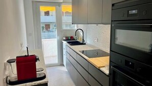 A modern kitchen with a built-in oven, a sink, and a red appliance on the countertop. - Viva Riviera Large 3 Bedrooms with balcony (Cannes)