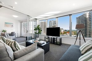 A modern living room with a large TV, comfortable seating, a coffee table, and a view of high-rise buildings.