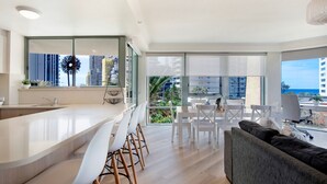 A modern apartment with a kitchen, dining area, and living room. It features large windows with city views and a balcony. - Family Fun at Sun City 3BR Near Beach - CoastHM (Surfers Paradise)
