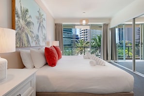 A hotel room with a large bed, a view of palm trees, and a balcony with a view of the city. - Family Fun at Sun City 3BR Near Beach (Surfers Paradise)