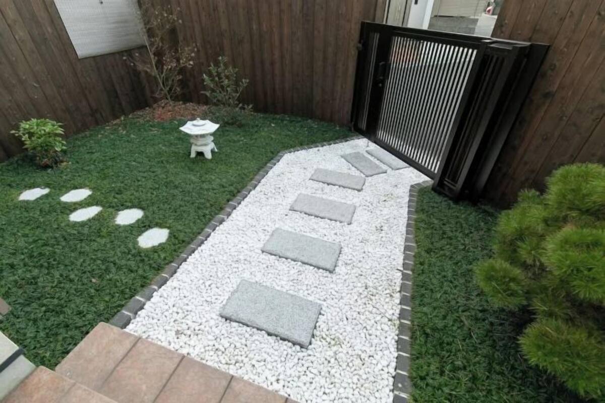 A garden with a stepping stone path, a small white statue, and a wooden fence.