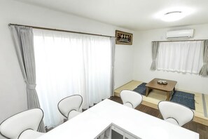 A room with a dining table, four chairs, a small sofa, a coffee table, and an air conditioning unit.