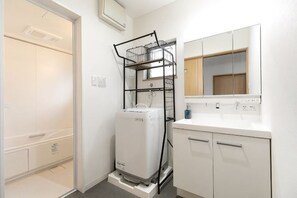 A compact bathroom with a white sink, mirror, and a stacked washer-dryer unit.