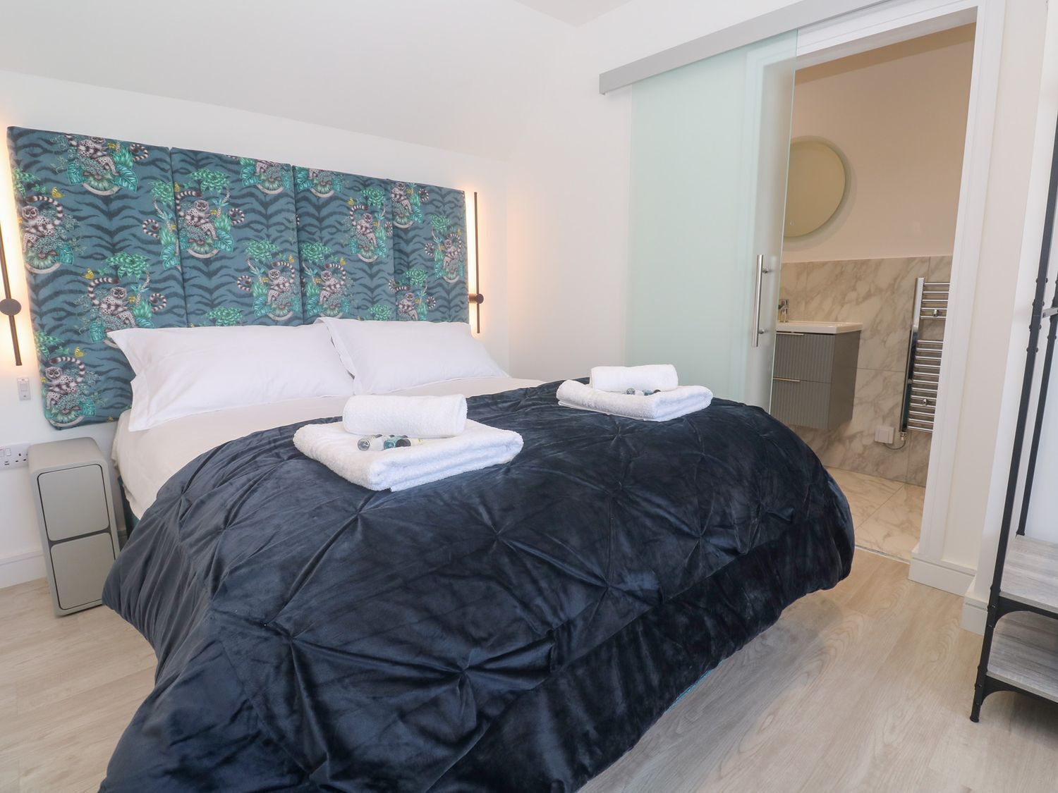 A hotel room with a large bed, two white towels, a patterned headboard, and a bathroom visible through an open door.