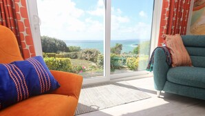 Una habitación con un amplio ventanal corredero que da a un balcón con vistas al mar y al verdor.