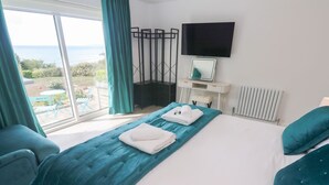 Habitación de hotel con una cama grande, un televisor montado en la pared y vistas al mar por la ventana.