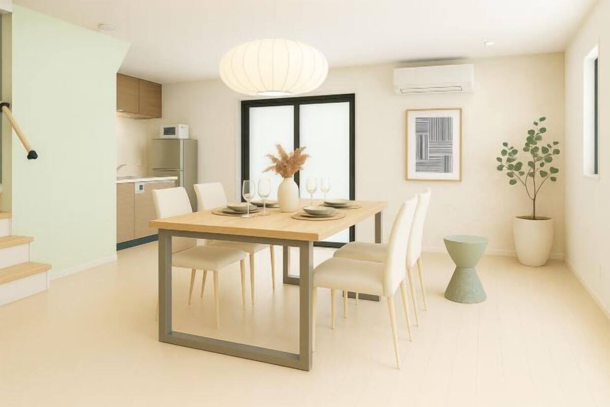 Un comedor moderno con una mesa de madera, sillas blancas, un jarrón con flores secas y una lámpara colgante.