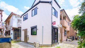 A two-story residential building with a white exterior, a small front porch, and a visible air conditioning unit. - Hana House Tokyo - Private House (Tokyo)