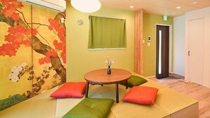 A room with tatami mats, a round table with a vase, and a wall with a tree painting. - Hana House Tokyo - Private House (Tokyo)