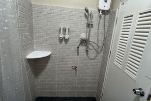 Une salle de bain avec des murs recouverts de carreaux blancs, un espace douche, un lavabo et une porte dotée d’une fenêtre.
