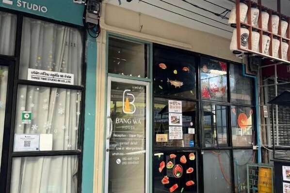 Une devanture de magasin avec une porte vitrée, une enseigne indiquant « BANG WA HOUSE », et divers produits alimentaires exposés à l’extérieur.
