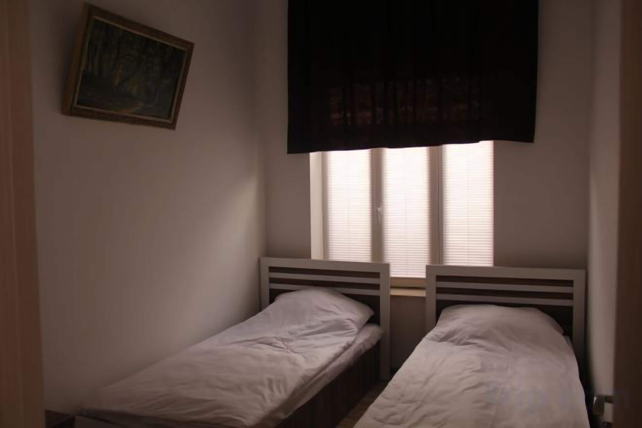 Quarto com duas camas de solteiro, janela com persianas e um quadro na parede.