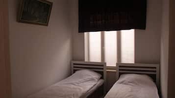 Quarto com duas camas de solteiro, janela com persianas e um quadro na parede.