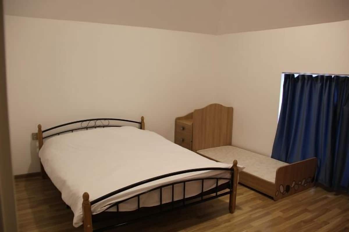 A single bed with a wooden frame and a mattress, a bedside table, and a window with blue curtains.