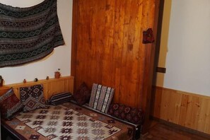 A room with a wooden wall, a bed with patterned bedding, and a hanging tapestry. - Colour (Baku)