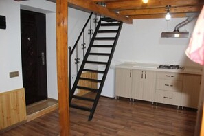 A kitchen with wooden cabinets, a stove, and a black metal staircase. - Colour (Baku)