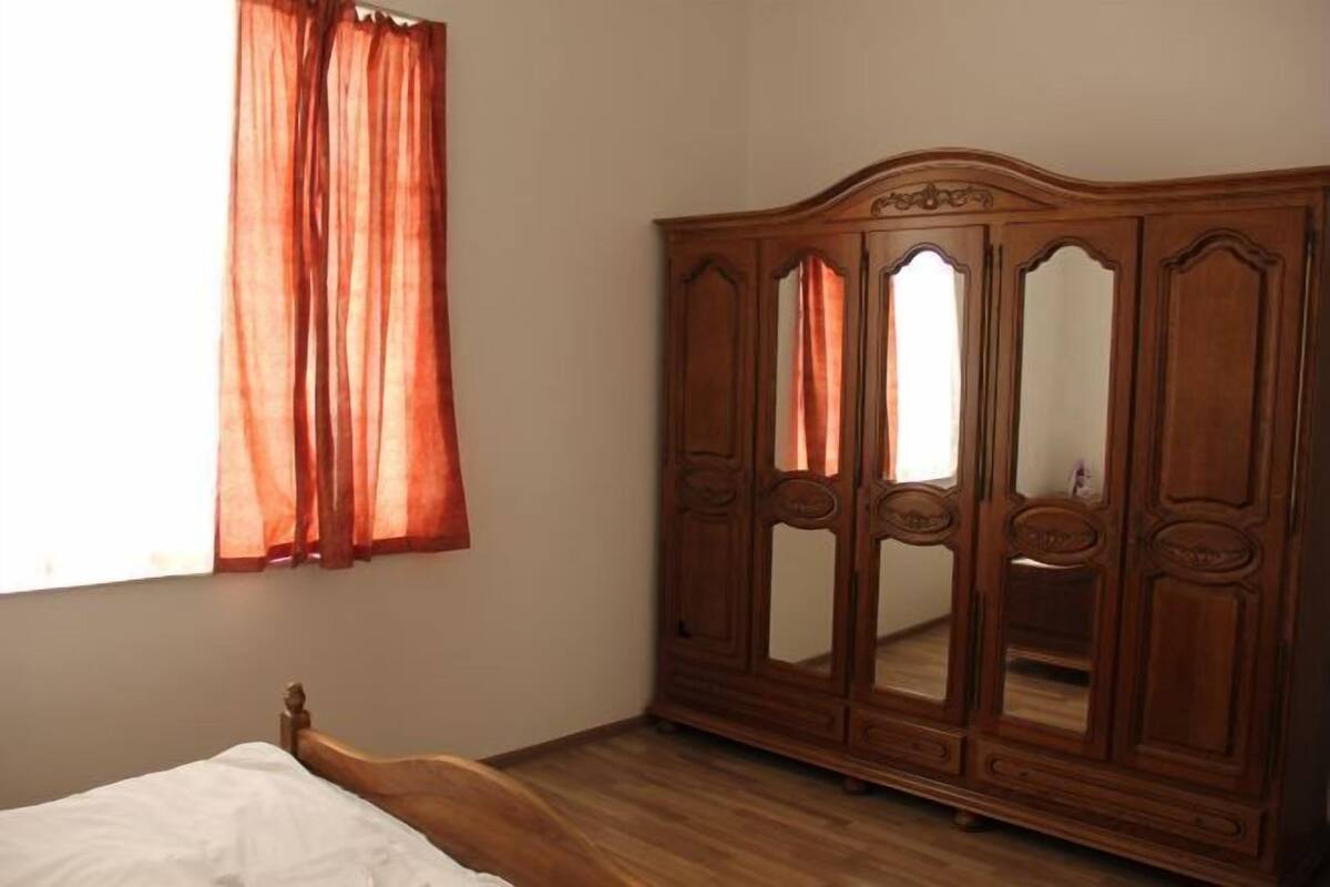 A bedroom with a wooden bed, a wardrobe with mirrored doors, and a window with curtains.