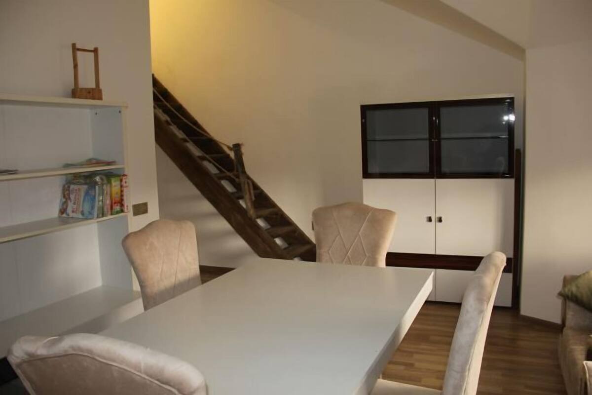 A dining area with a table and chairs, a staircase, and a wardrobe with a window.