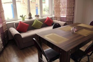 A dining area with a wooden table, chairs, and a sofa with colorful cushions. - Colour (Baku)
