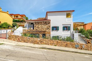 Une maison à deux étages avec une façade en pierre, un mur en pierre à l’avant et une allée pavée.