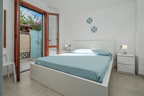 A bedroom with a bed, a nightstand, a chair, and a shower area.